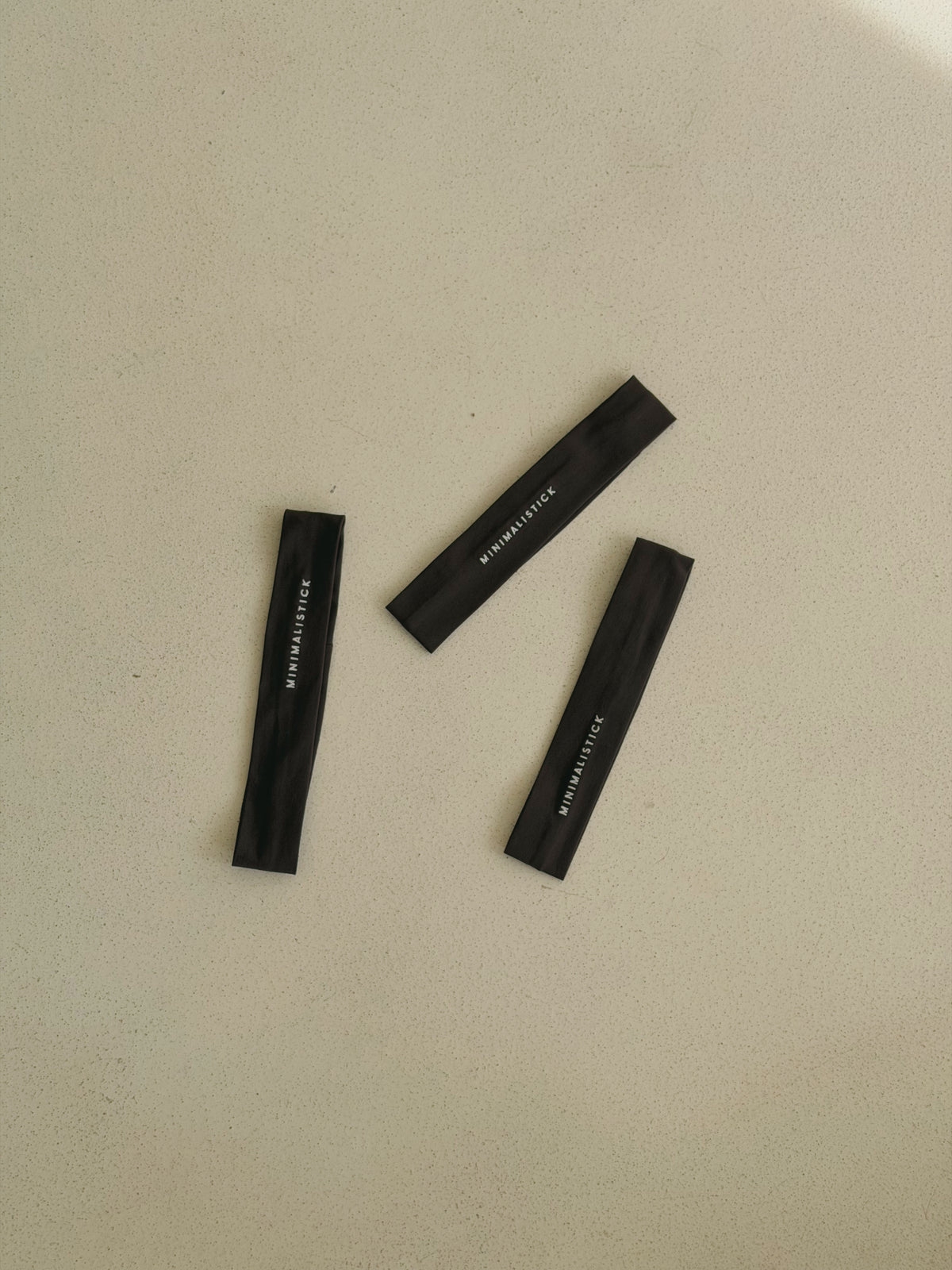 Tři tmavé sportovní čelenky z organické bavlny s logem MINIMALISTICK, položené na světlém pozadí.