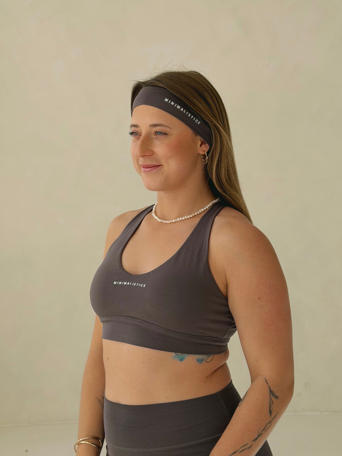 Tmavě šedá sportovní čelenka z organické bavlny s logem MINIMALISTICK na modelce, pohled z poloprofilu.